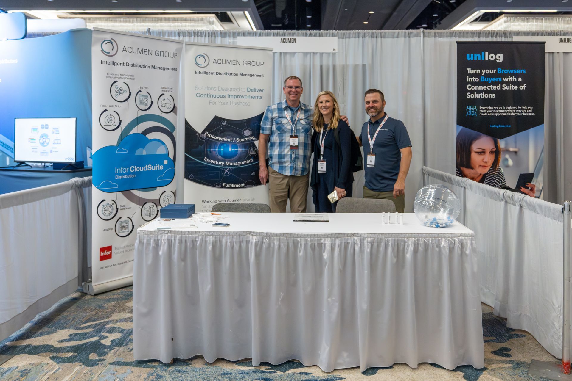 Three people at a trade show booth with banners promoting Unilog cloud solutions.