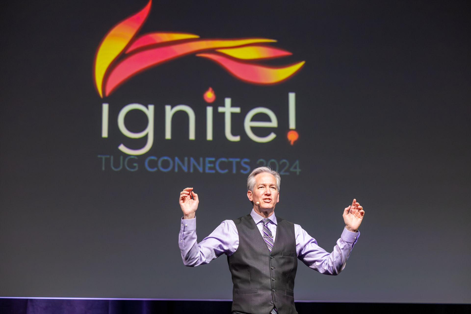 Man on stage with arms raised, presenting at 