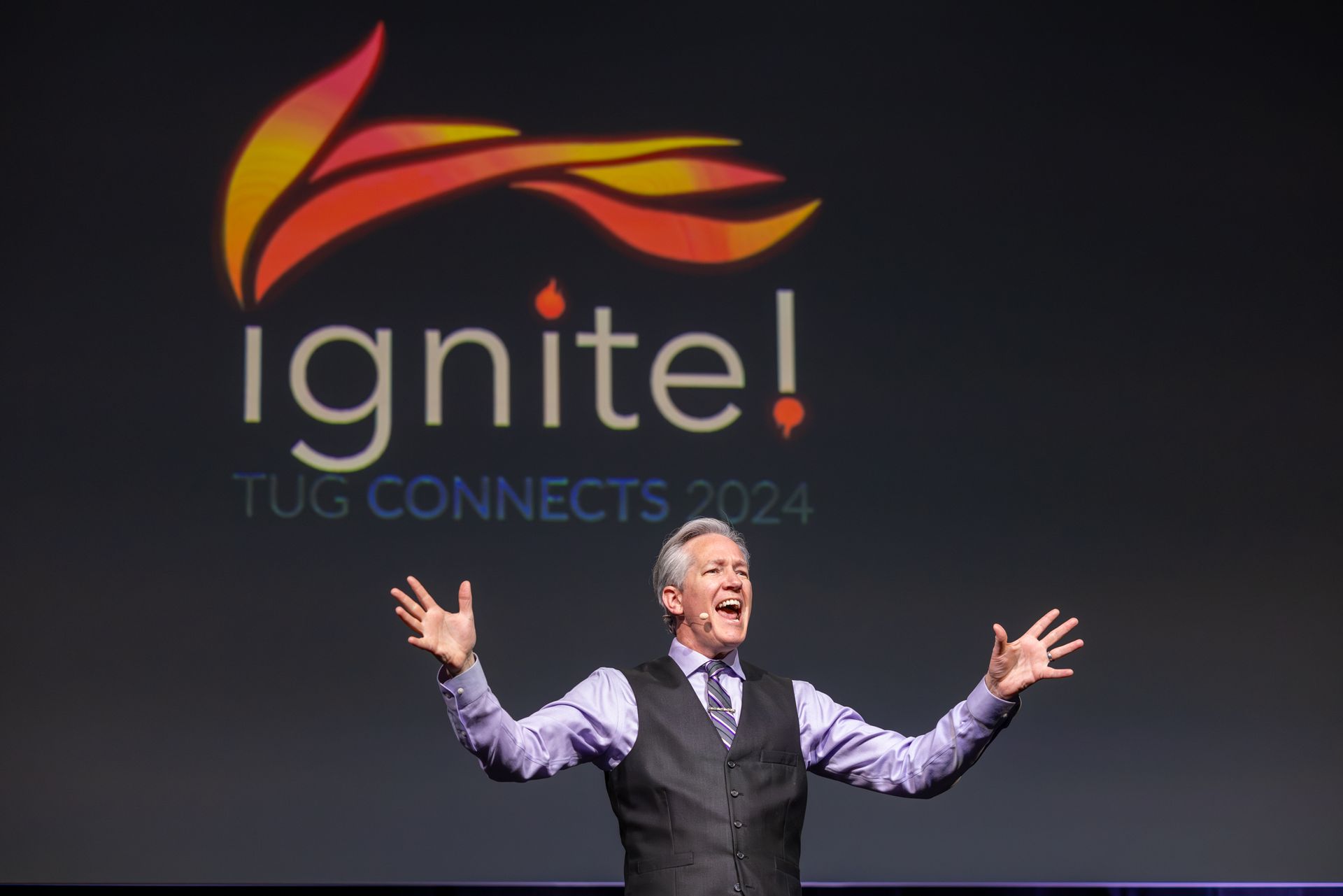 Man on stage with arms raised in front of 