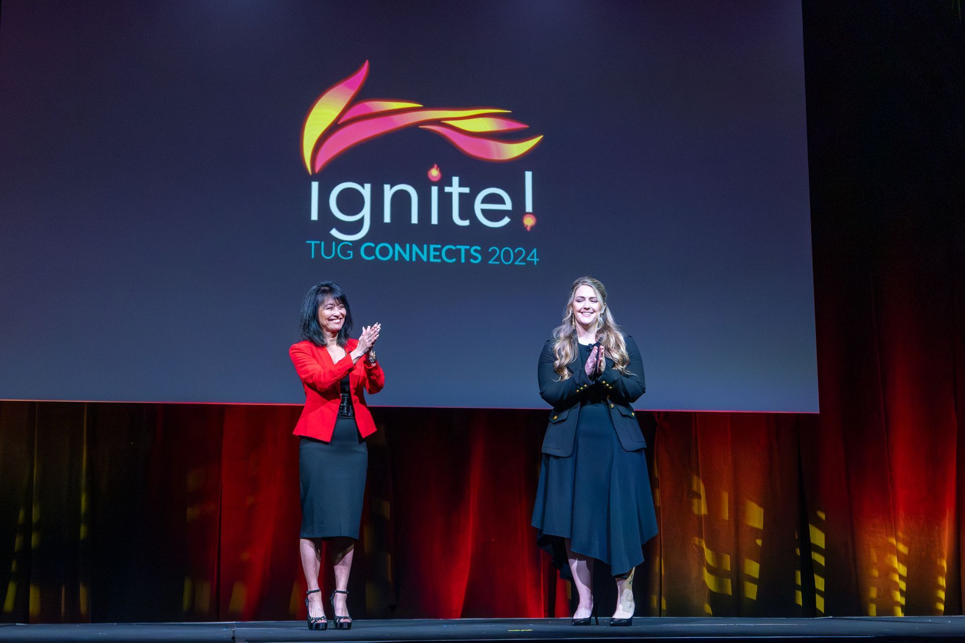 Two women on stage clapping under a 