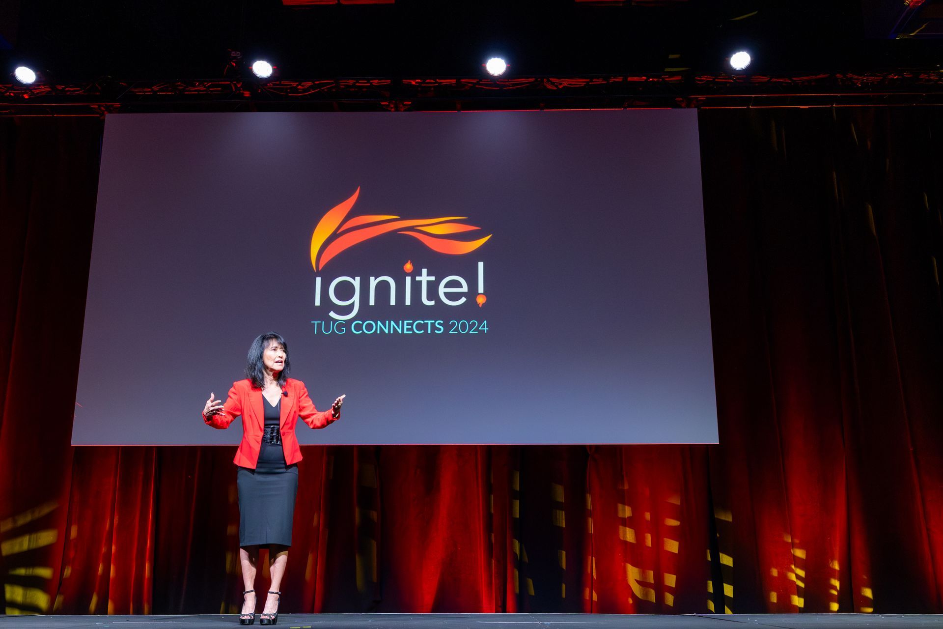 Woman in red blazer speaks on stage with 