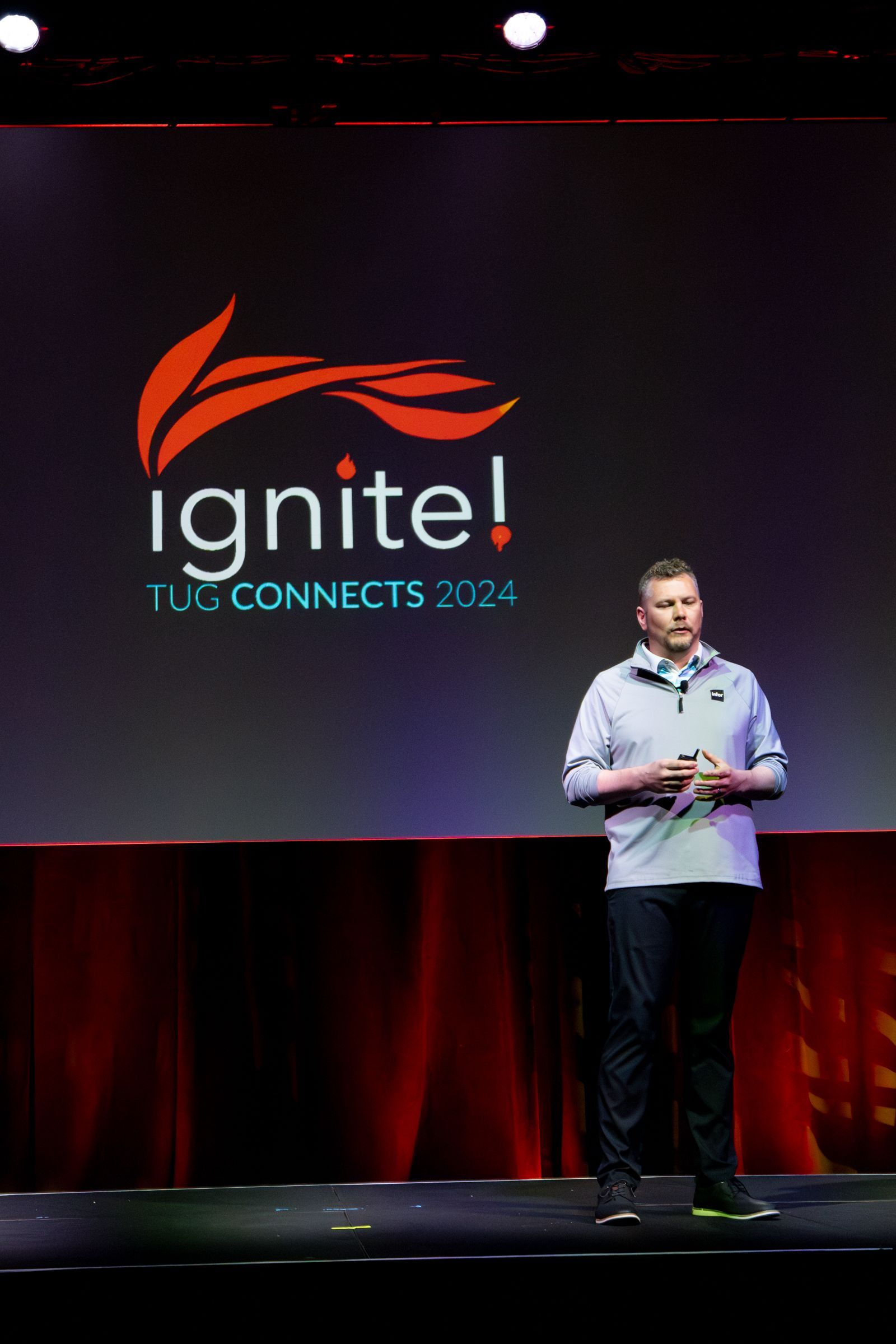 Man speaking on stage at the Ignite! Tech Connects 2024 conference, red and black background.