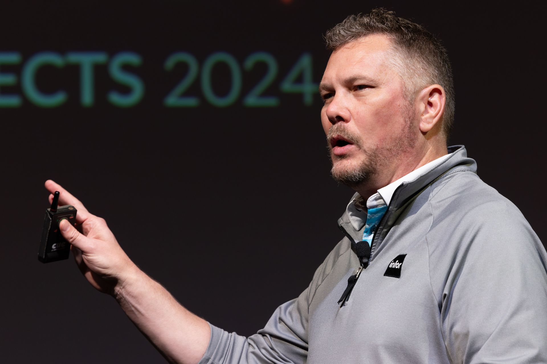 Man in gray shirt gestures, speaking at a presentation; 