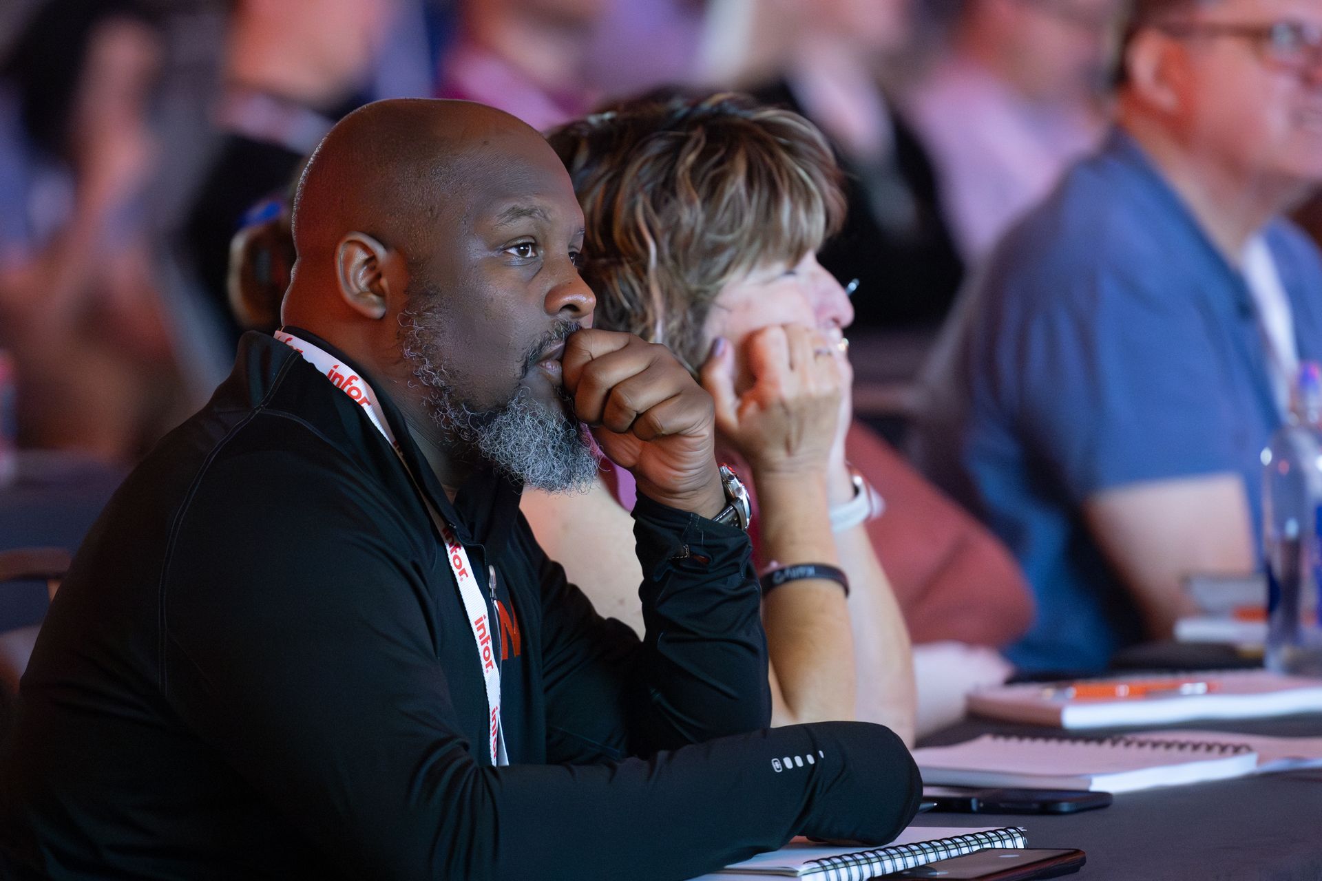 Man and woman attentively listening at a conference table, in an audience.