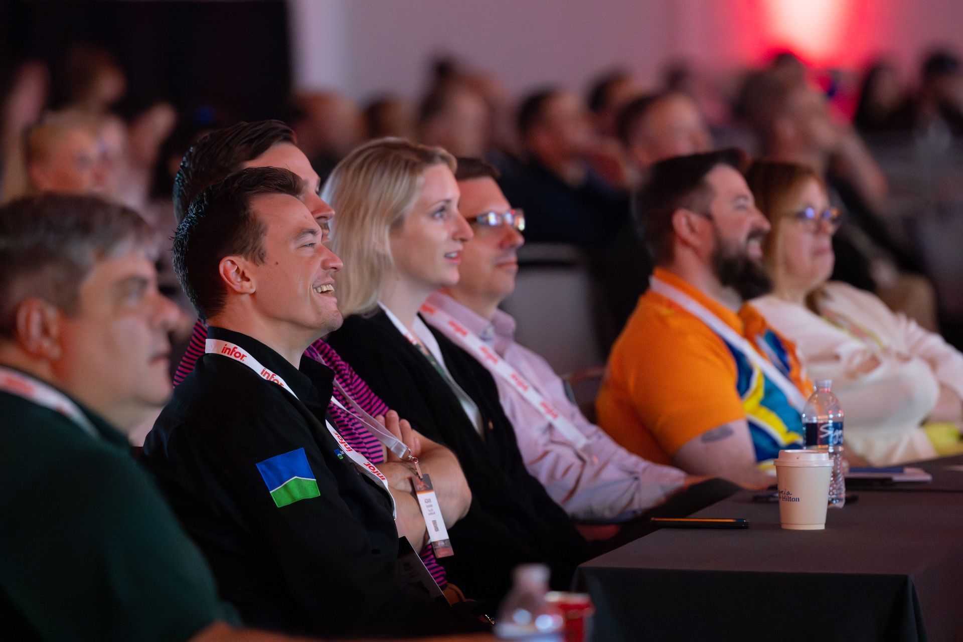Audience members seated at a conference, some smiling, focused on something off-screen.