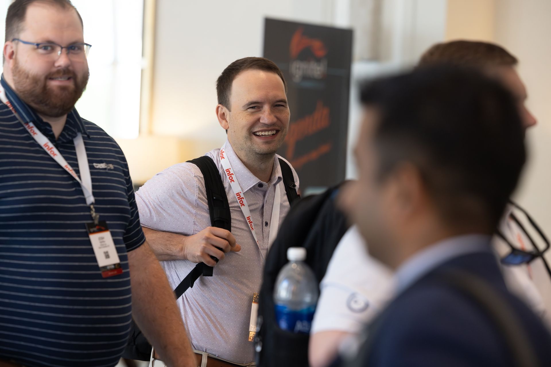 Attendees at a conference, smiling, some wearing lanyards, interacting in a well-lit hallway.