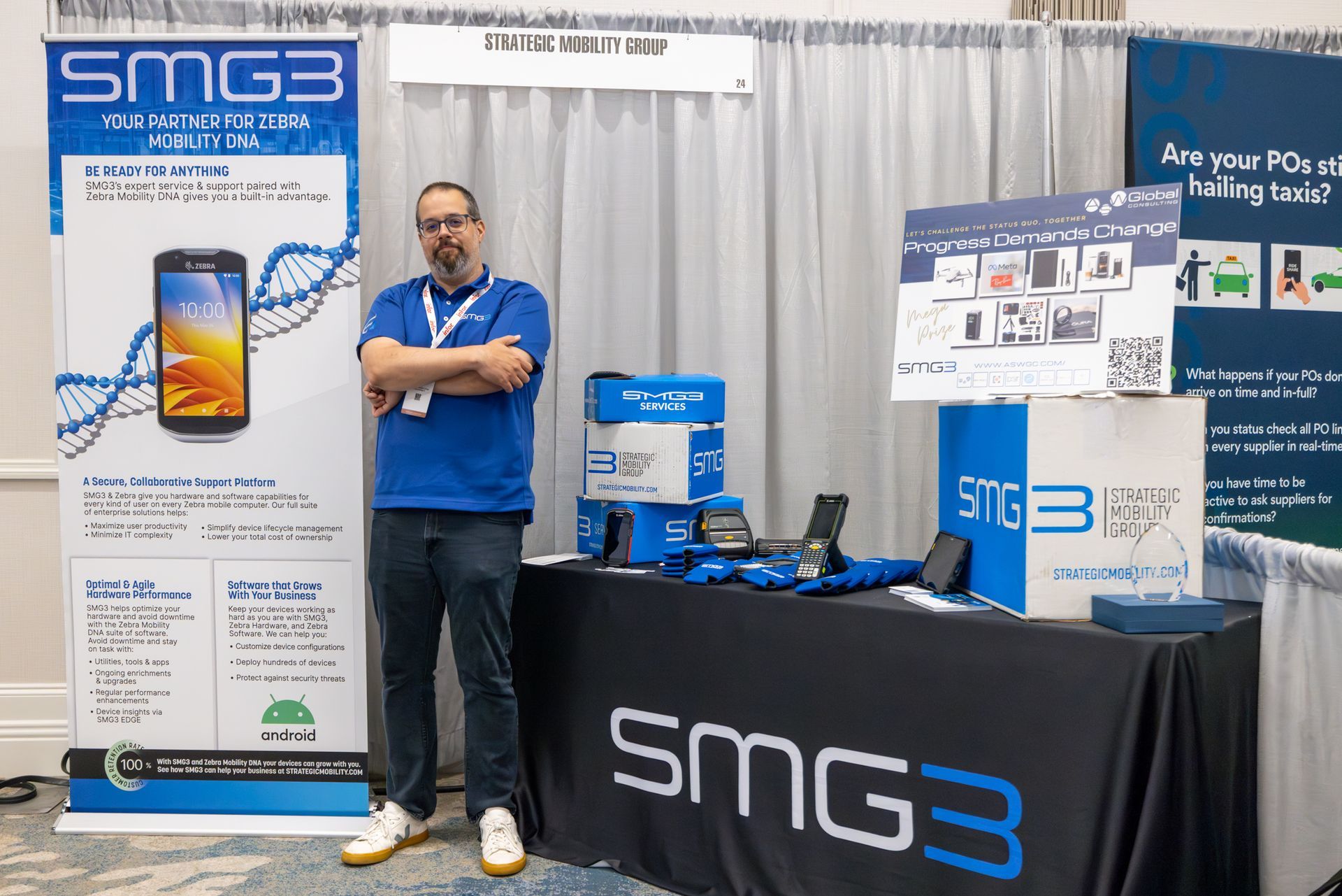 Man stands by SMG3 booth; displays include a phone, boxes, and a banner.