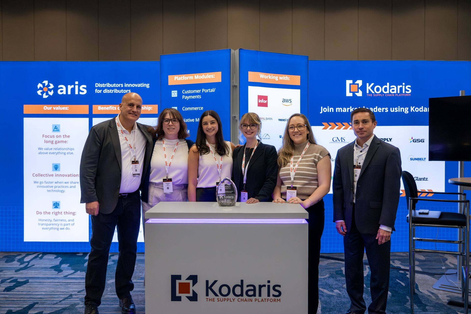People posing at a Kodaris booth, standing in front of a blue and white backdrop.
