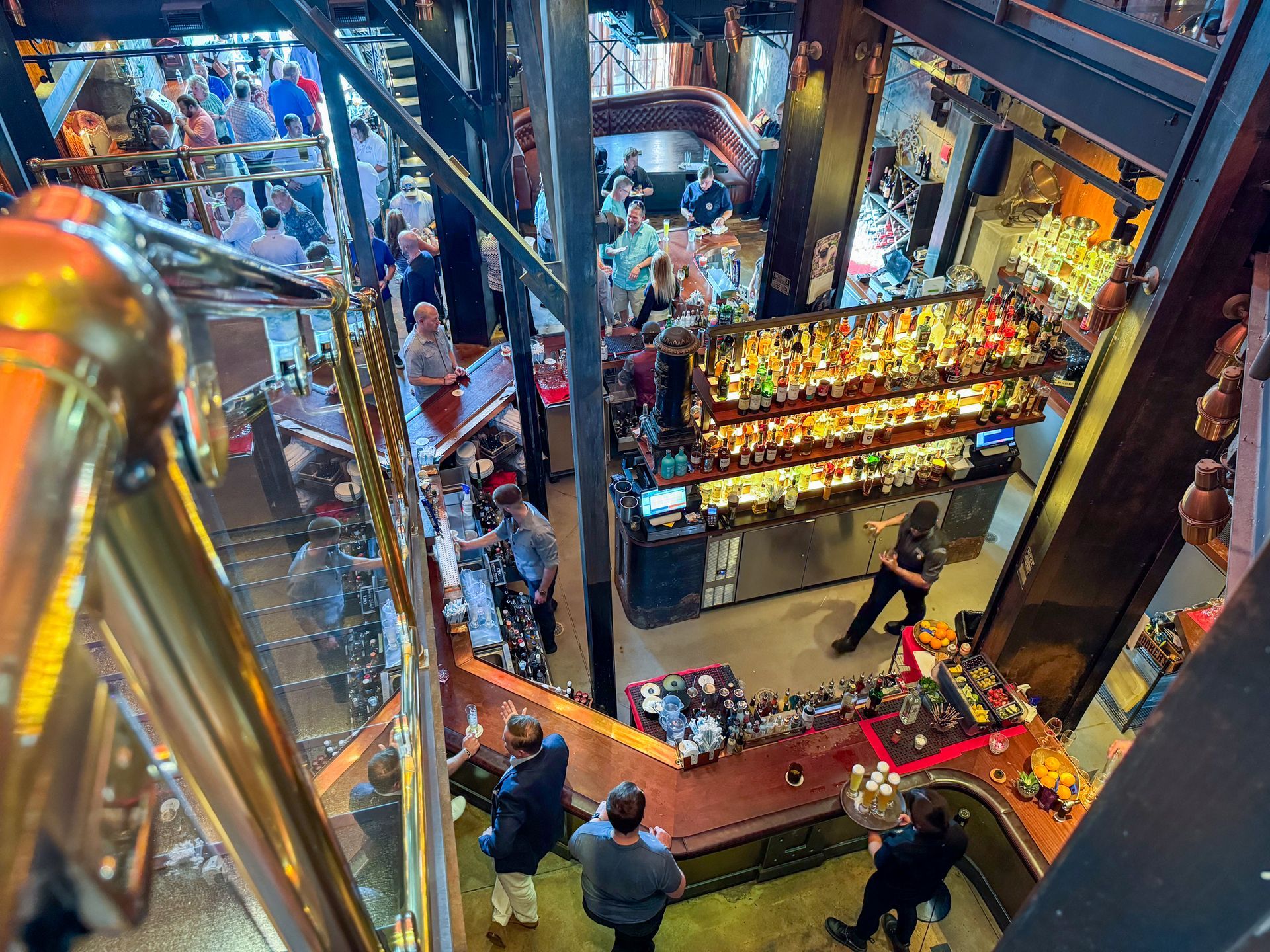 Interior view of a bar with people. Copper accents, multiple levels, and a well-stocked bar are visible.