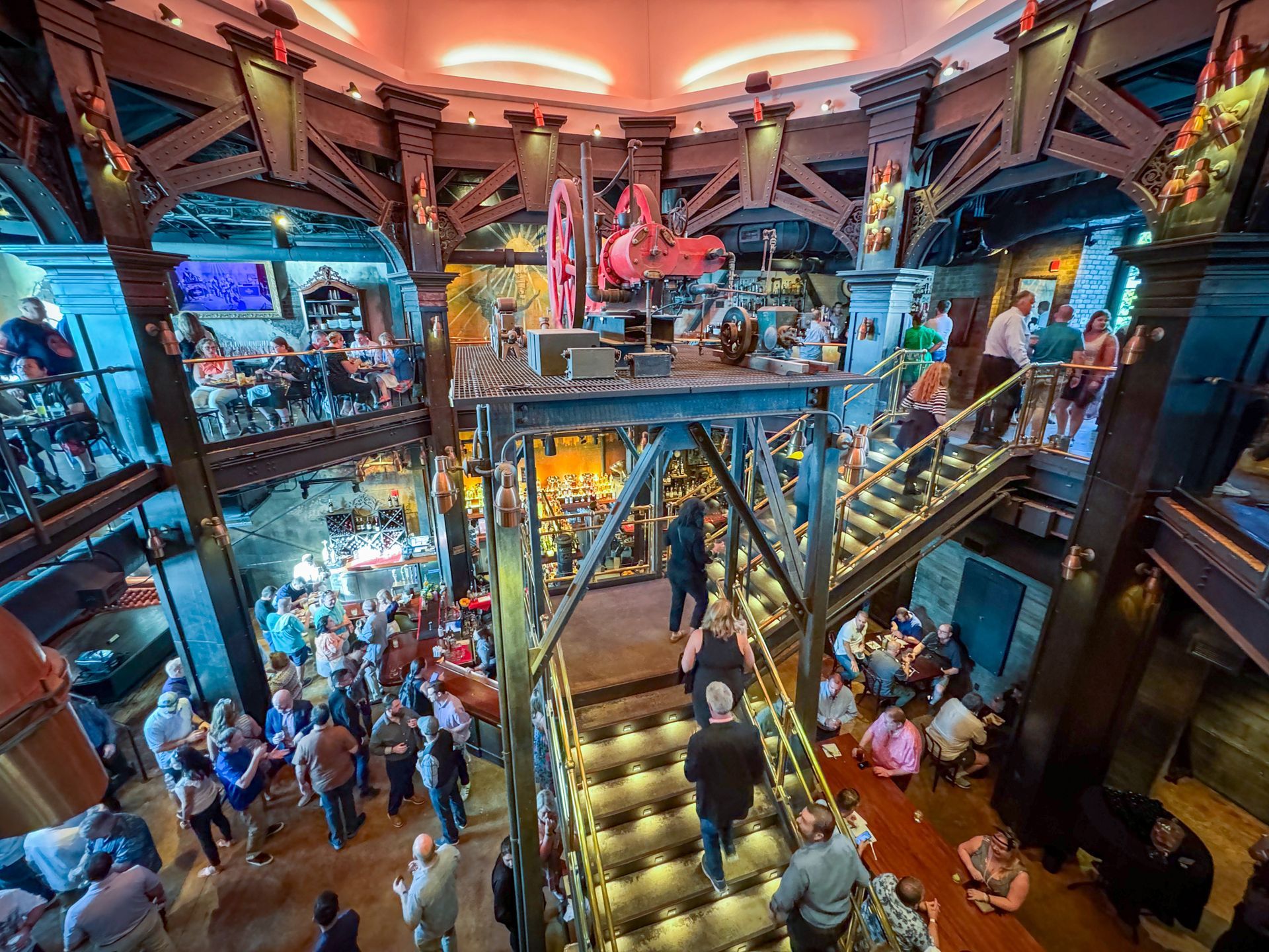 Interior view of a crowded restaurant with multiple levels, staircases, and a stage. People are present.