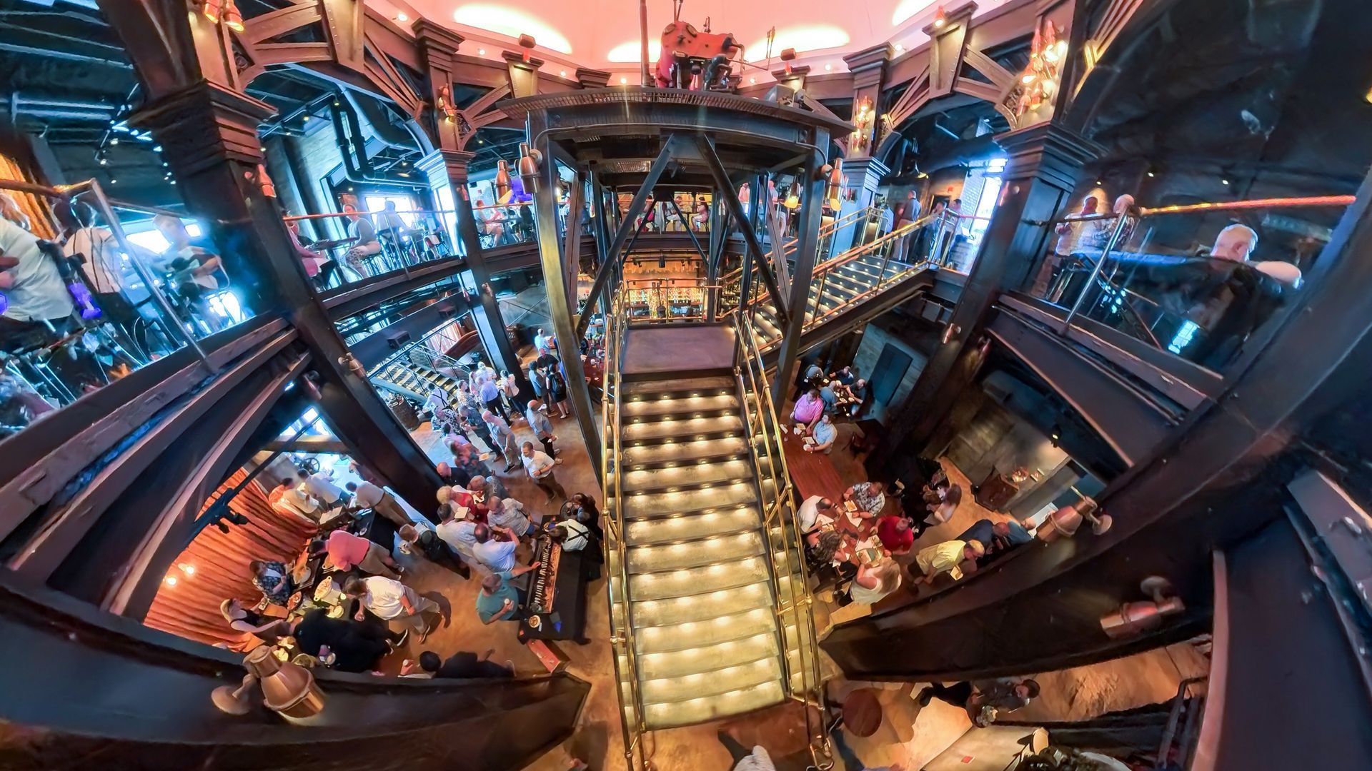 Multi-level interior of a bar with people at tables, metal staircases, and circular architecture.
