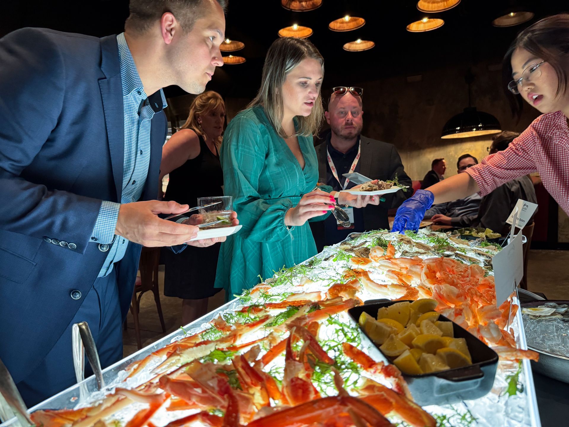 People selecting seafood from a buffet, served by a woman in a pink shirt.