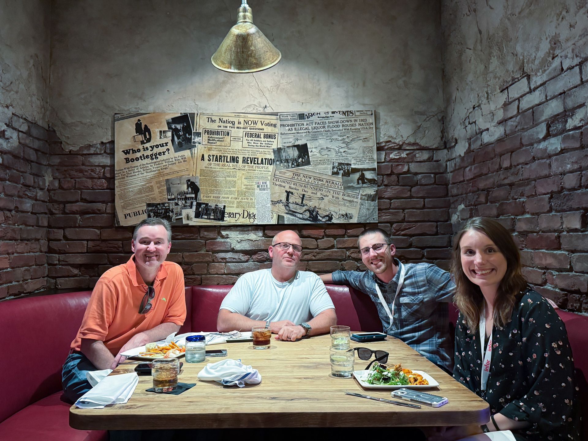 Four people seated at a table in a brick-walled booth. A light hangs overhead.