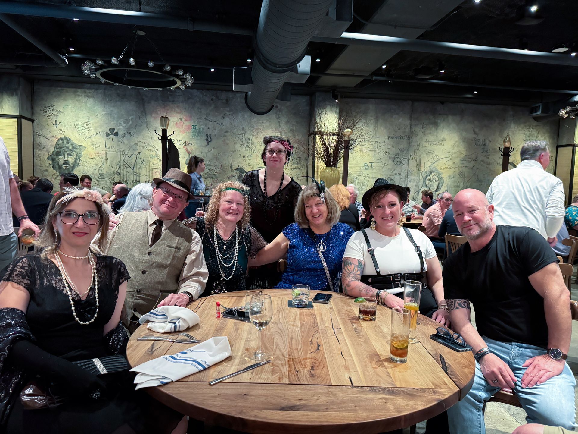 Group of people in vintage attire seated around a wooden table in a restaurant.