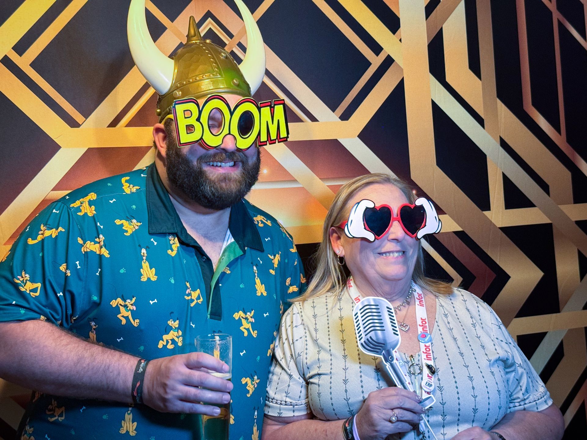 Two people with props smiling in a photo booth with a gold art deco backdrop.
