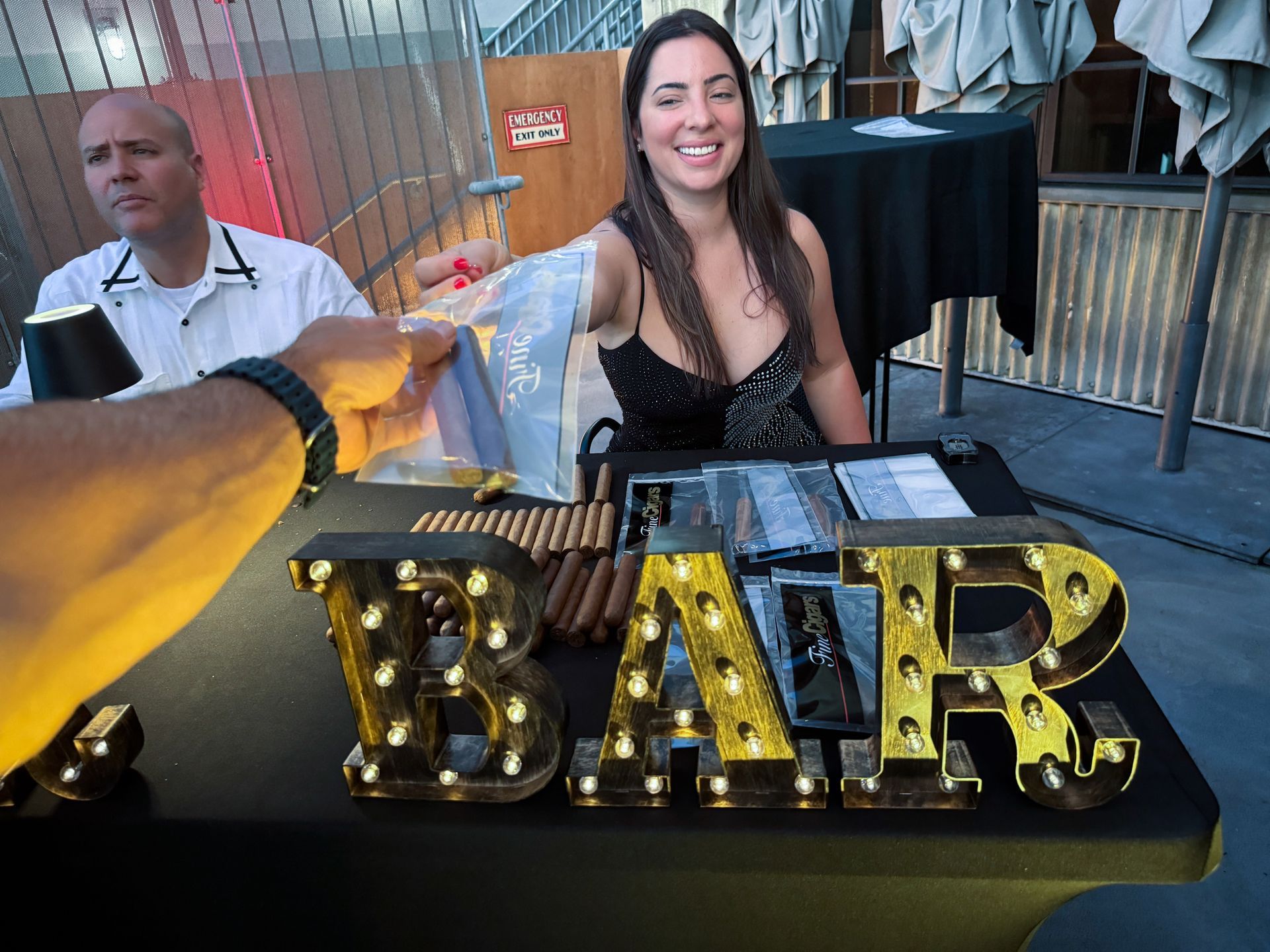 A woman smiles, handing a drink to a person at a bar with illuminated 