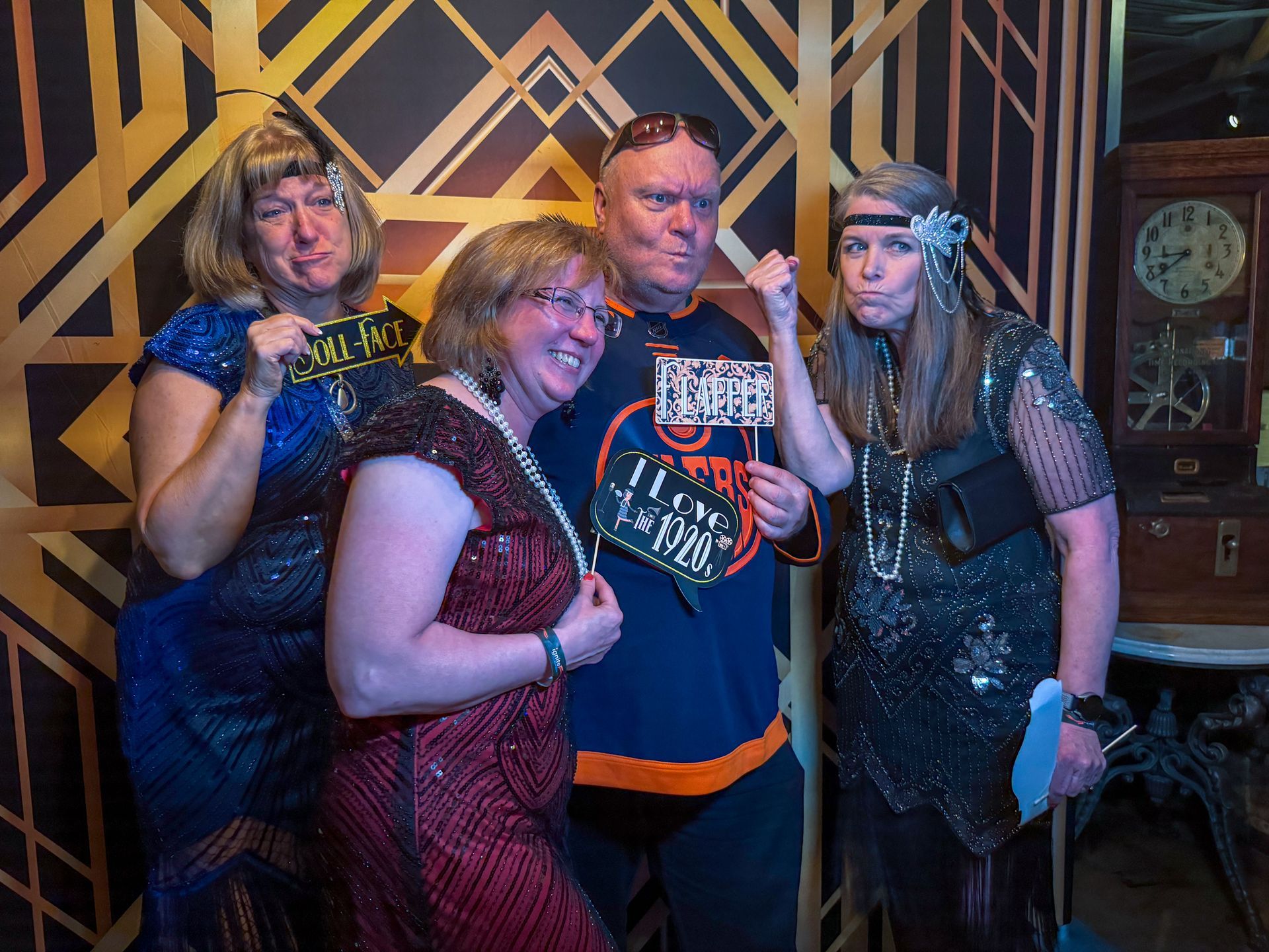 Four people in 1920s attire posing with props in front of a deco backdrop.