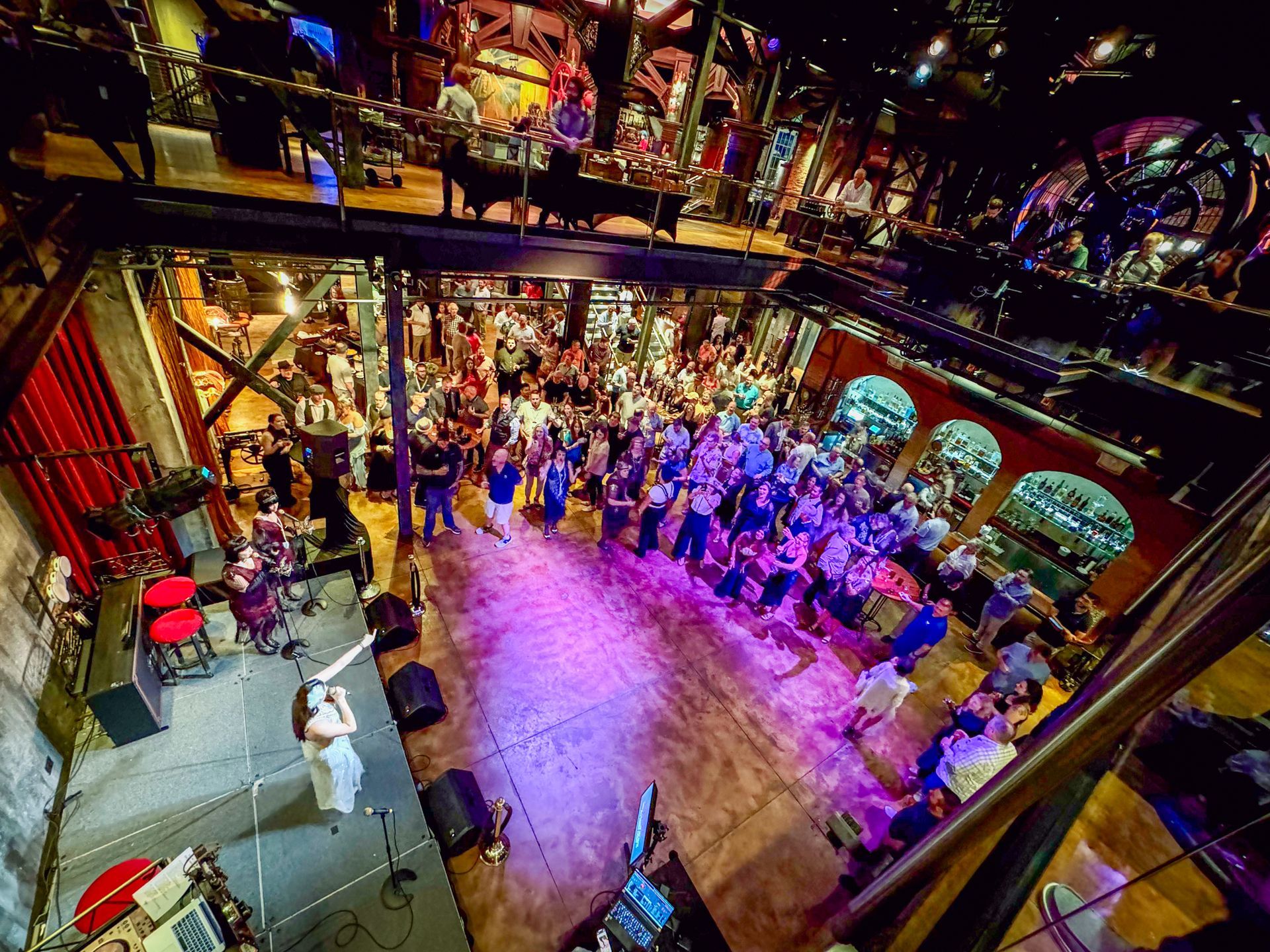 Audience watches a live performance in a multi-level venue with stage lights.