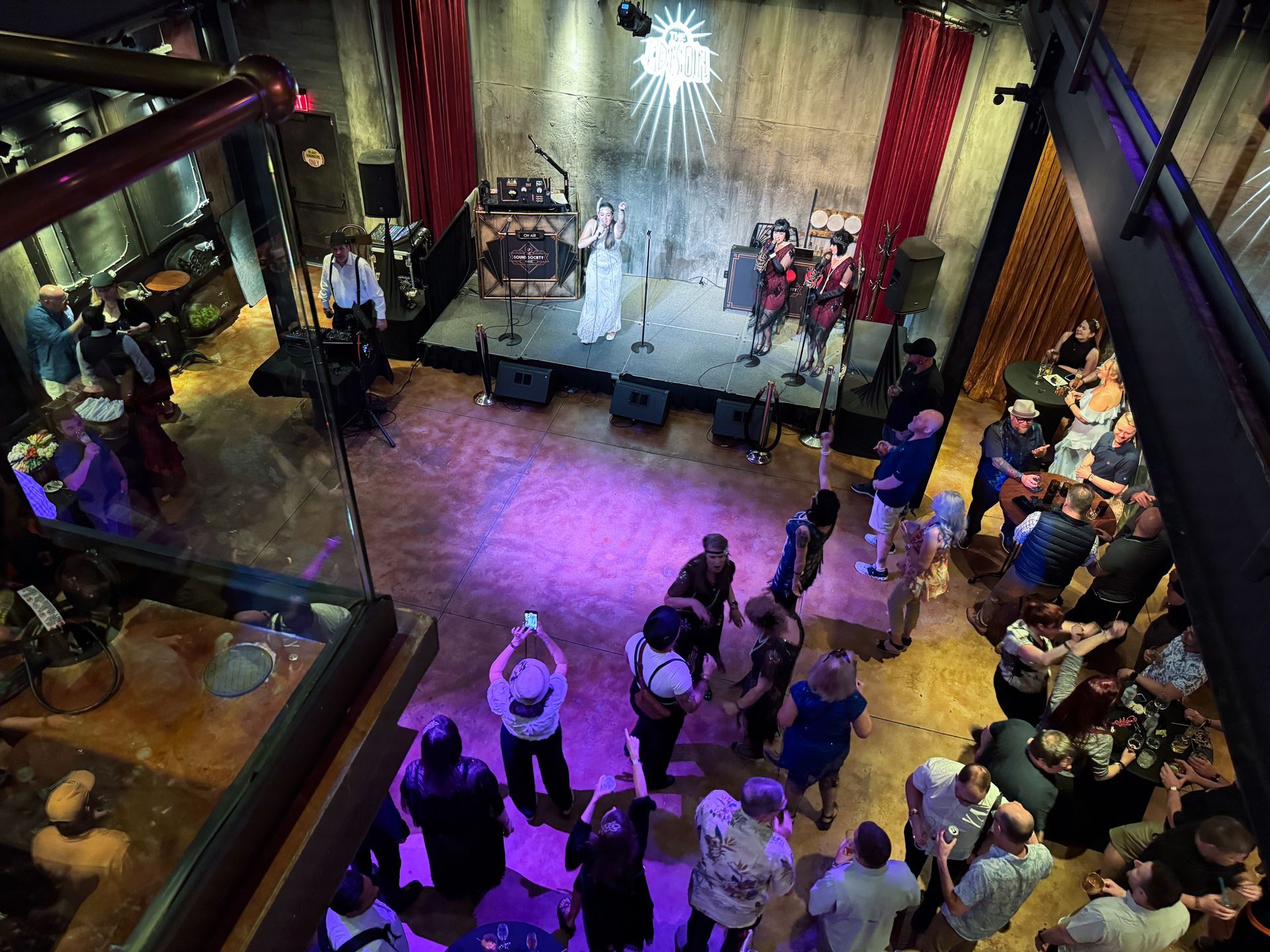 Band performing on stage in a dimly lit venue, people watching. Purple and red lighting.