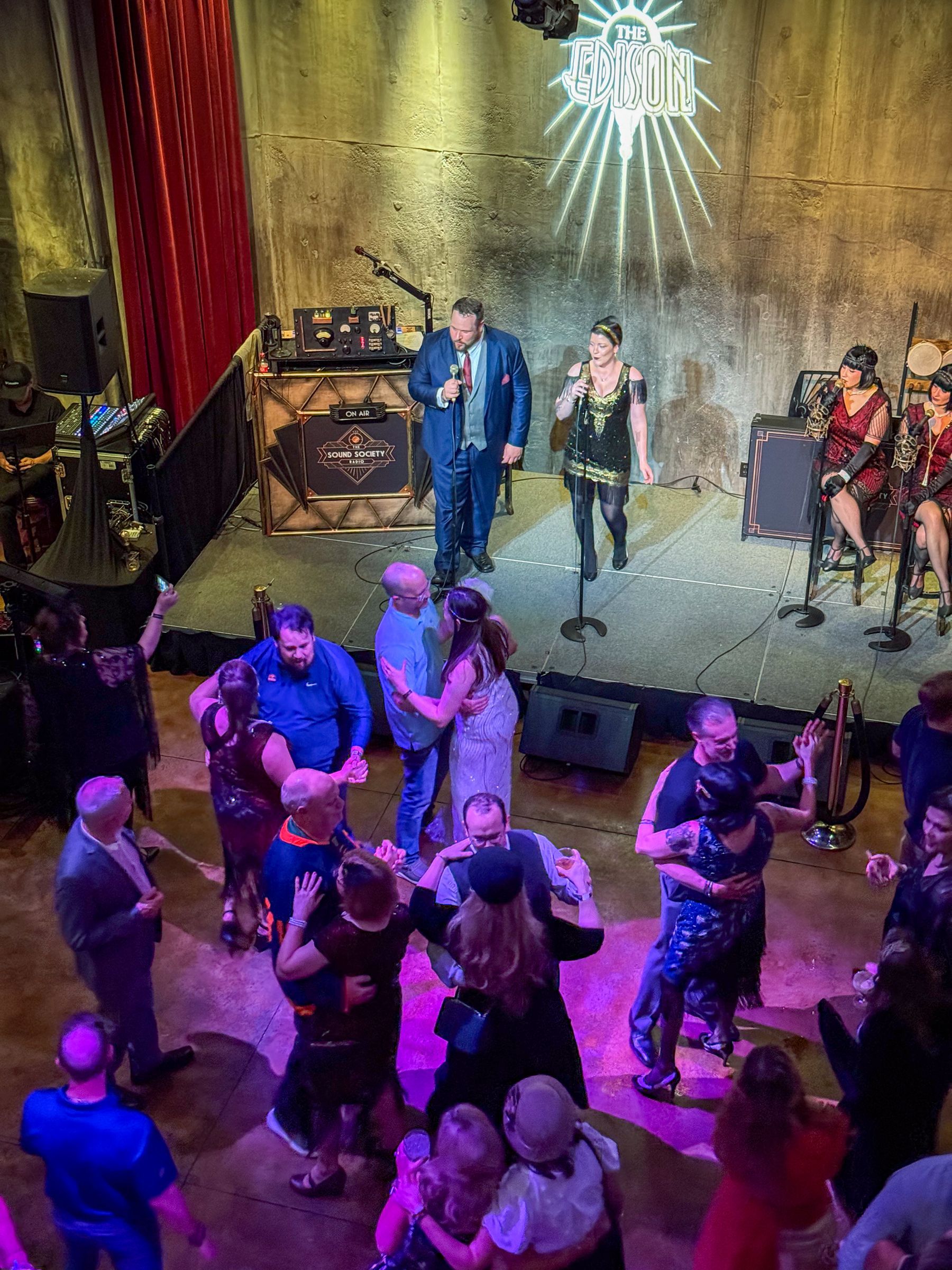 Band performs on stage as people dance at a venue with low lighting.