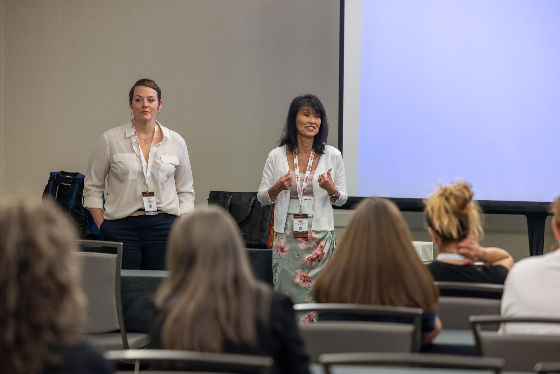 Two women giving a presentation in a conference room with an audience.