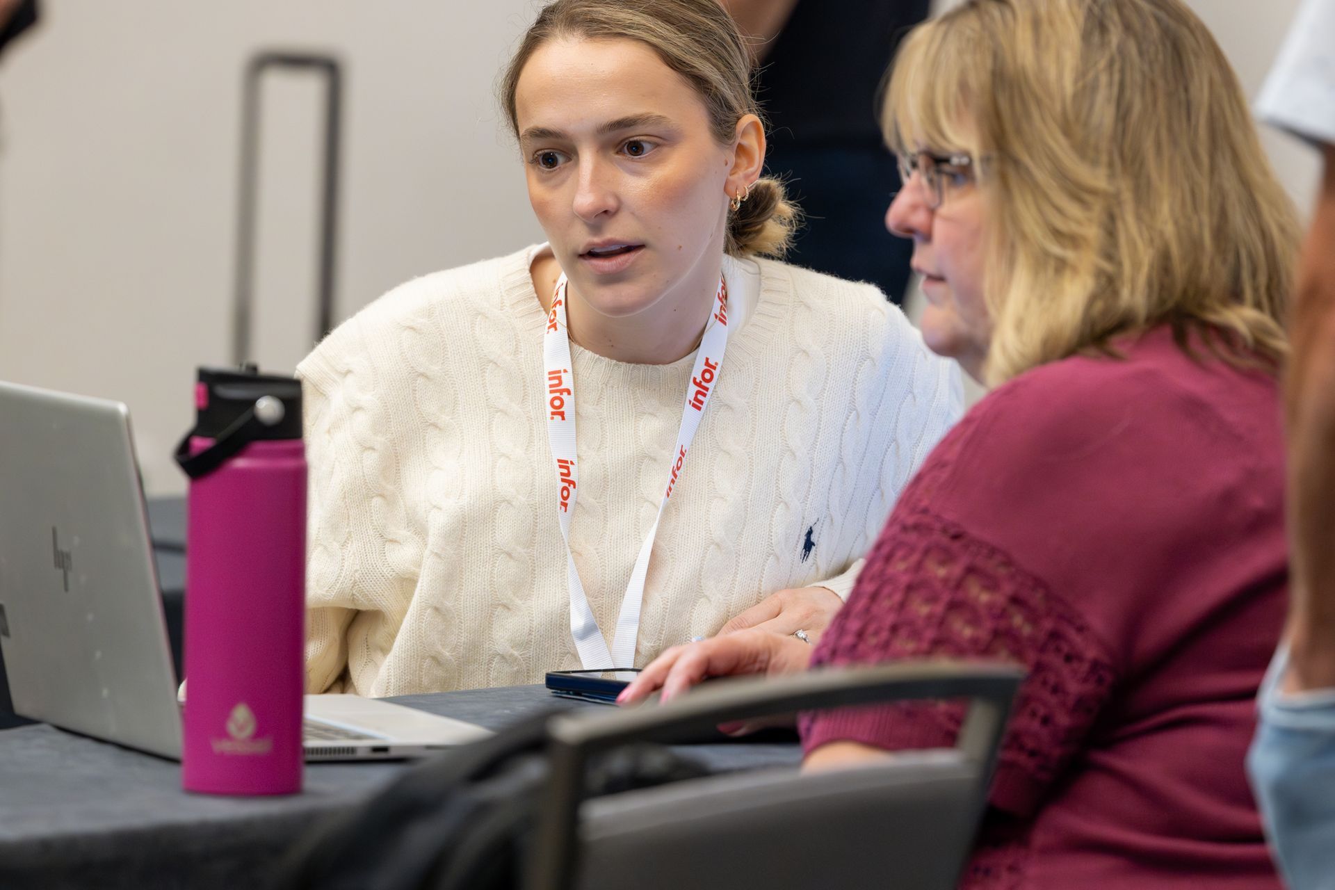Two women looking at a laptop, one wearing a cream sweater and the other a maroon shirt.