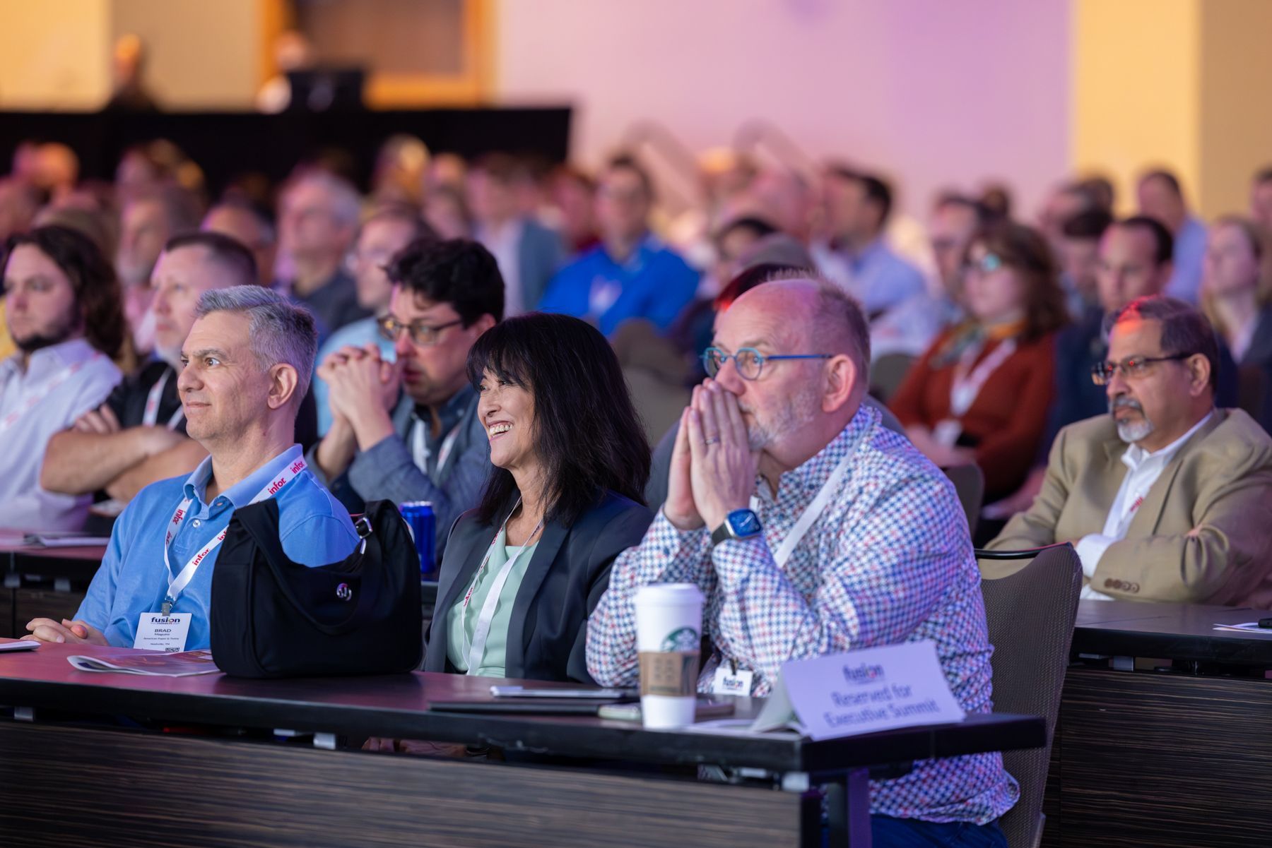 Audience in a conference room; people listening attentively. Some have hands on faces, others smiling.