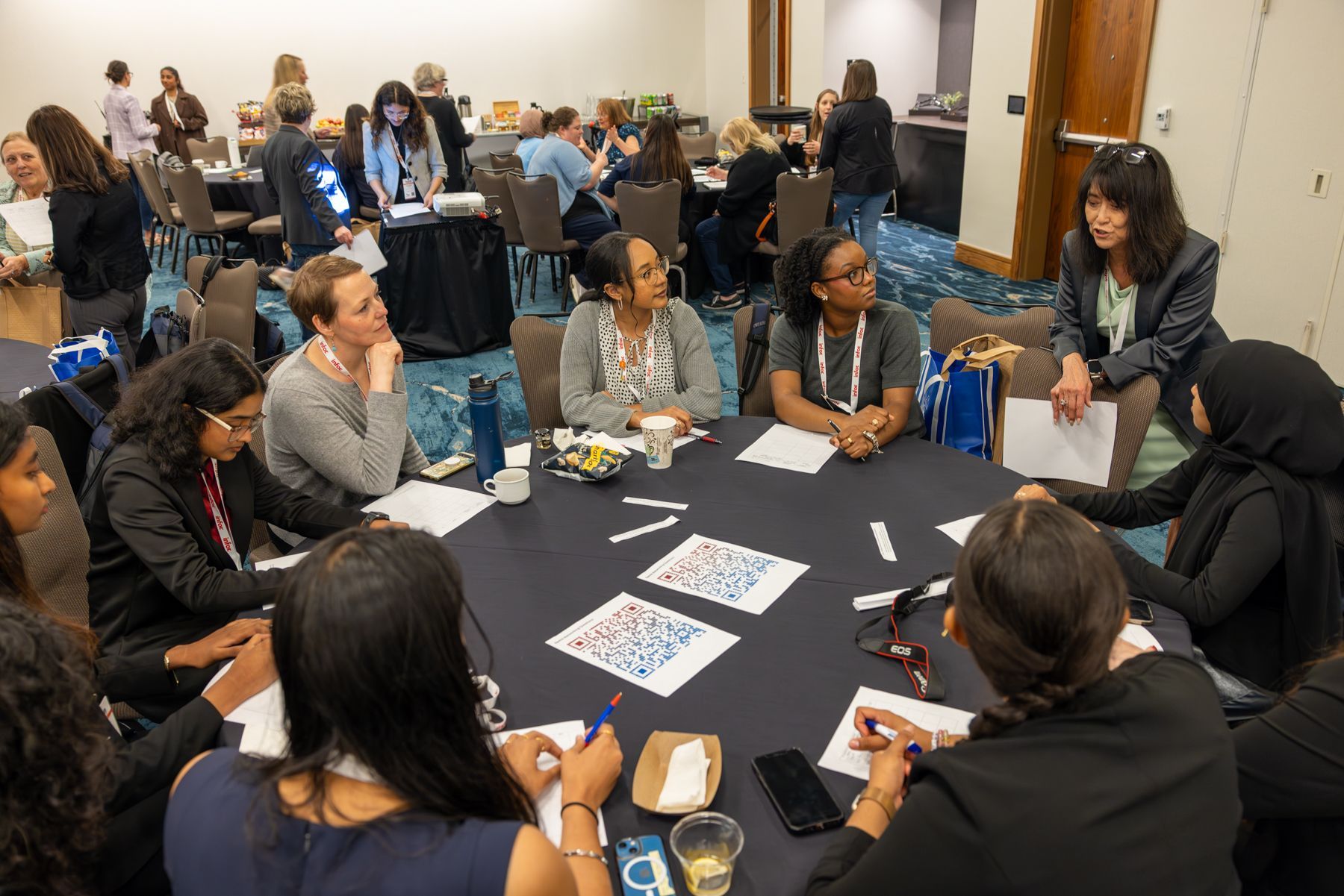 Group of people around a circular table in a conference room, engaged in discussion.