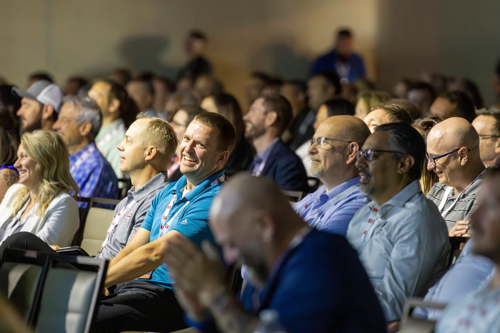 Audience in a conference room, smiling and listening. People are in the foreground and background.