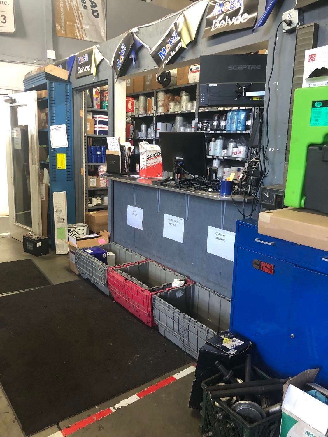 A store counter with shelves of items.  Bins line the front. A computer and monitor sit on the counter.