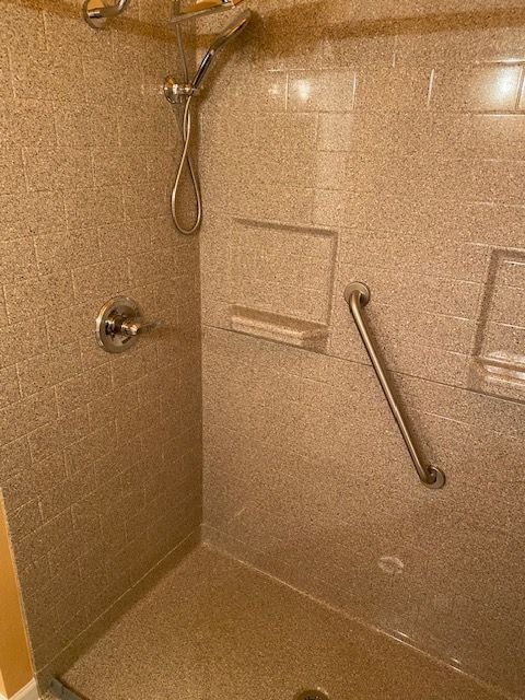 A walk in shower with a hand rail and a shower head.