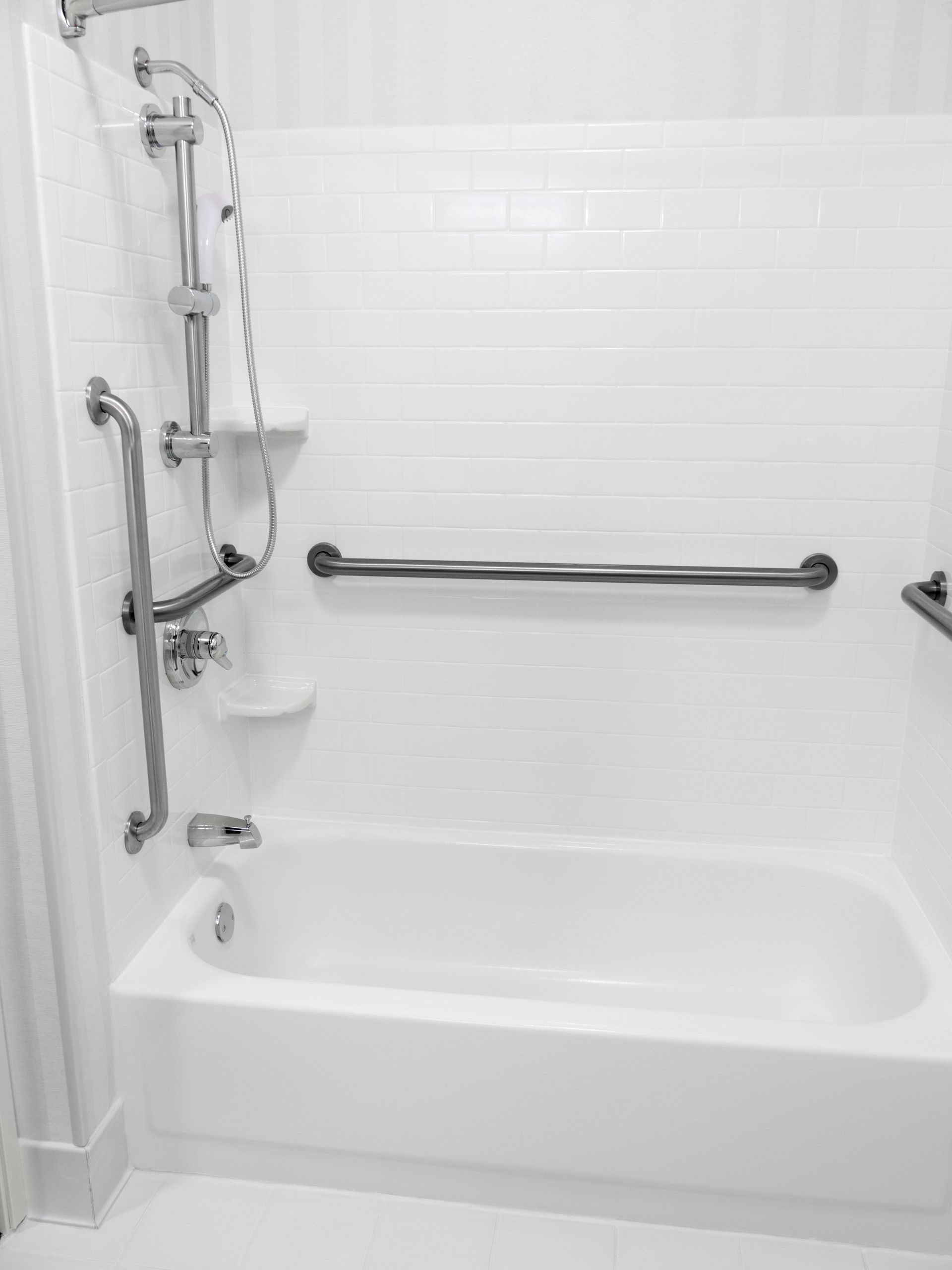 A white bathtub with stainless steel handles in a bathroom.