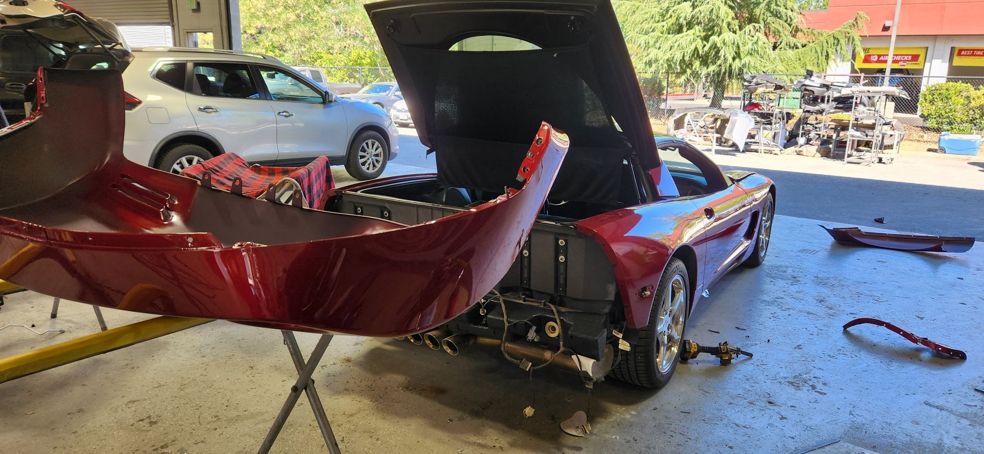Red sports car with front-end damage in a garage, hood open, bumper removed, and parts scattered nearby | Tripp's Auto Body