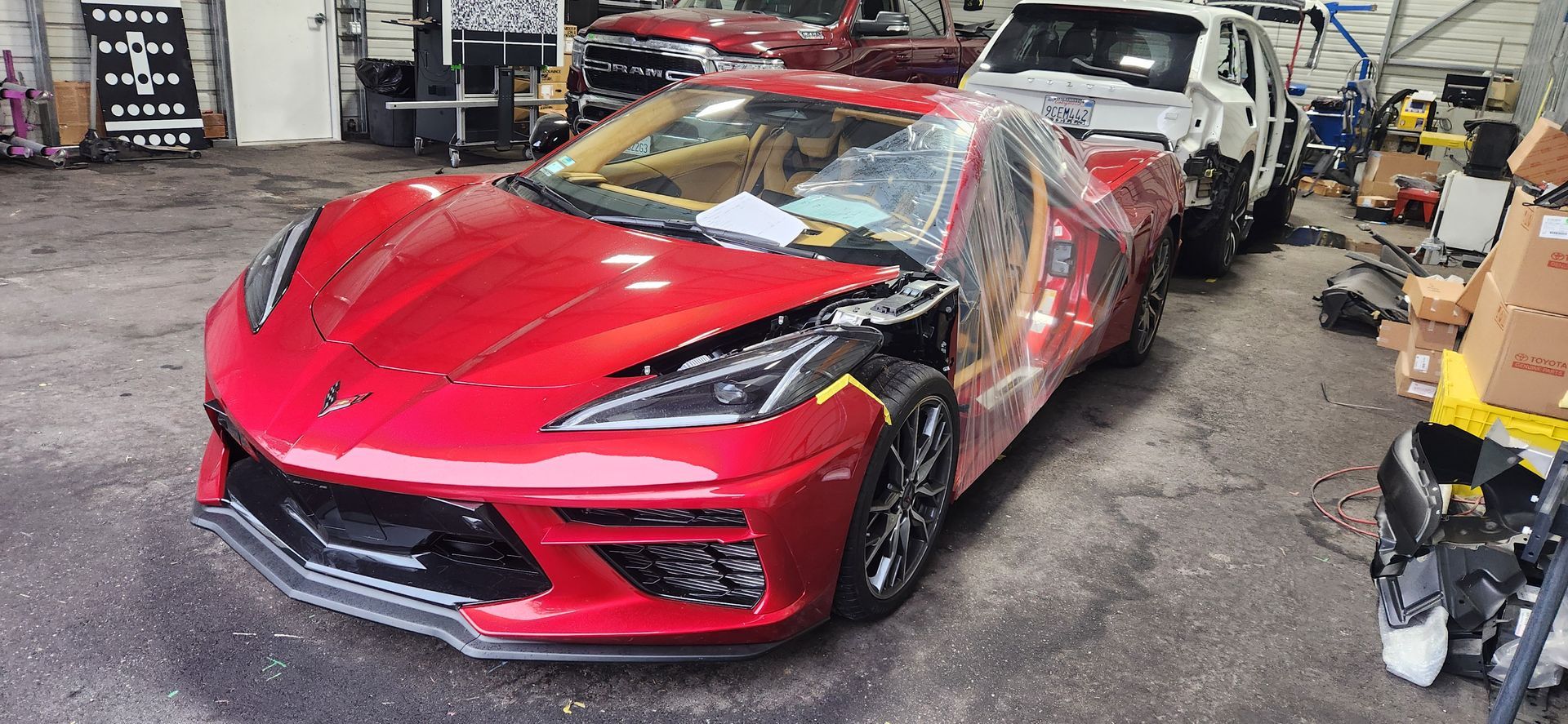 Red sports car wrapped in clear plastic inside a garage or body shop, with another car behind it. | Tripp's Auto Body
