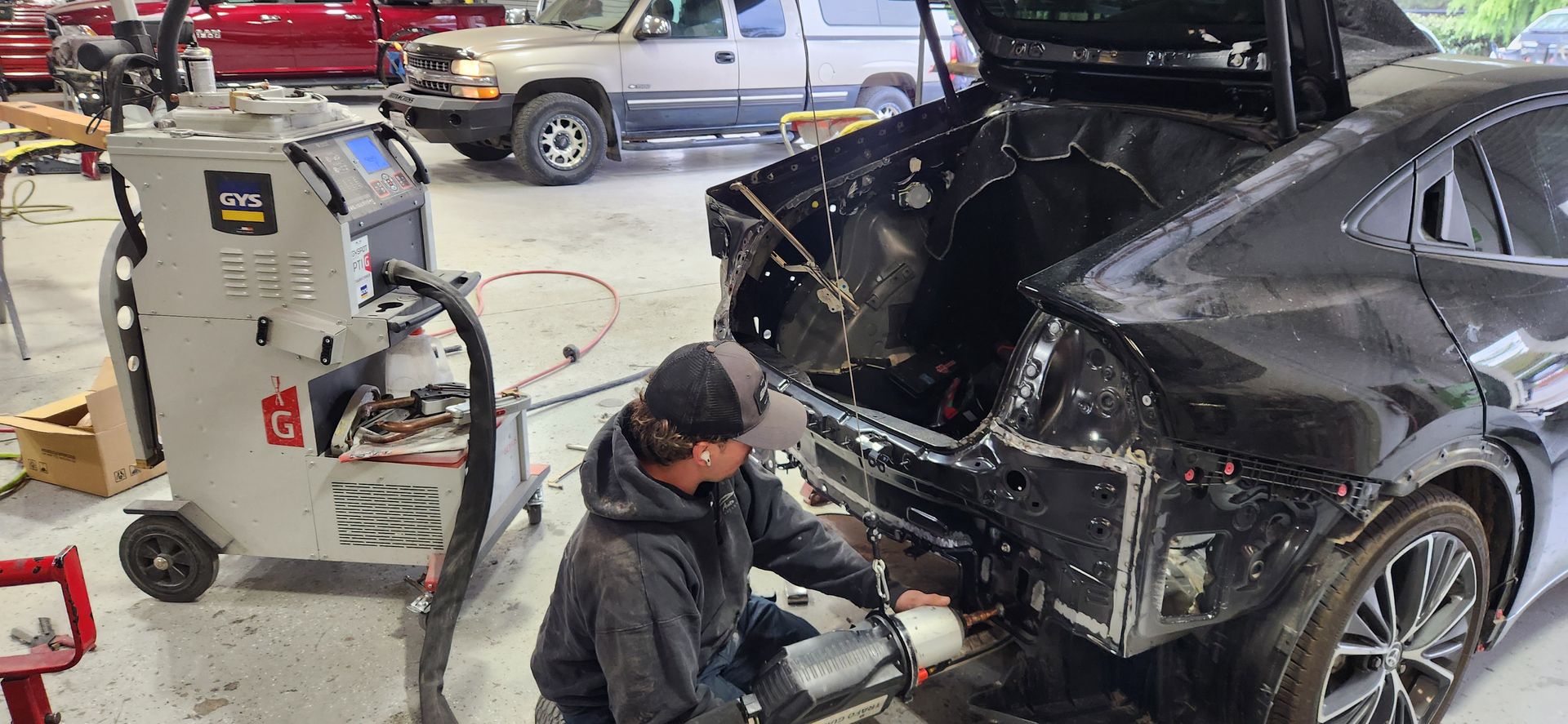 Mechanic working on the damaged rear of a black car in an auto repair shop | Tripp's Auto Body