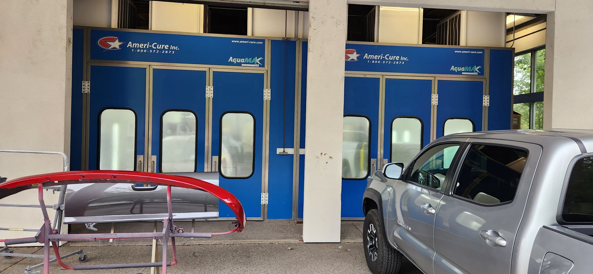 Auto paint bays with blue doors and parked vehicles under a covered drop-off area. | Tripp's Auto Body