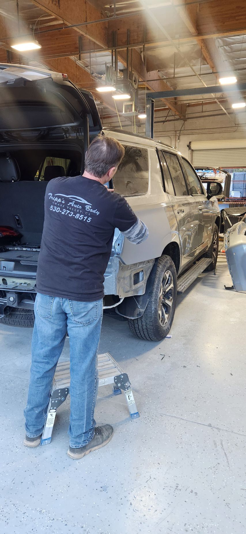 People working on a white SUV in an auto repair shop with the rear hatch open | Tripp's Auto Body