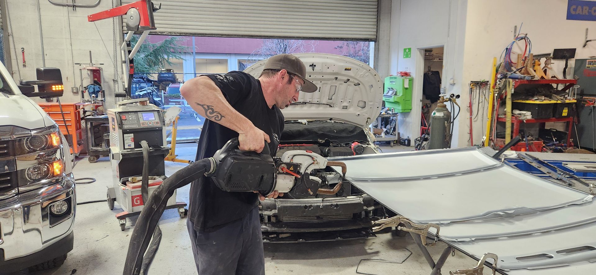 Technician vacuuming a car interior in an auto shop garage with tools and equipment nearby | Tripp's Auto Body
