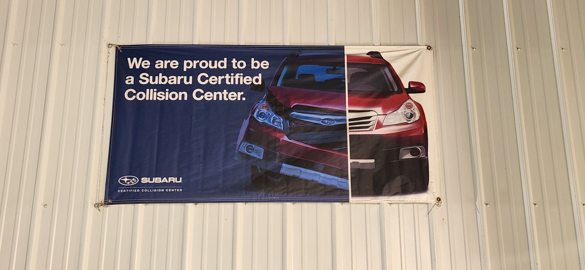Banner reading “We are proud to be a Subaru Certified Collision Center” on a wall with a car image | Tripp's Auto Body