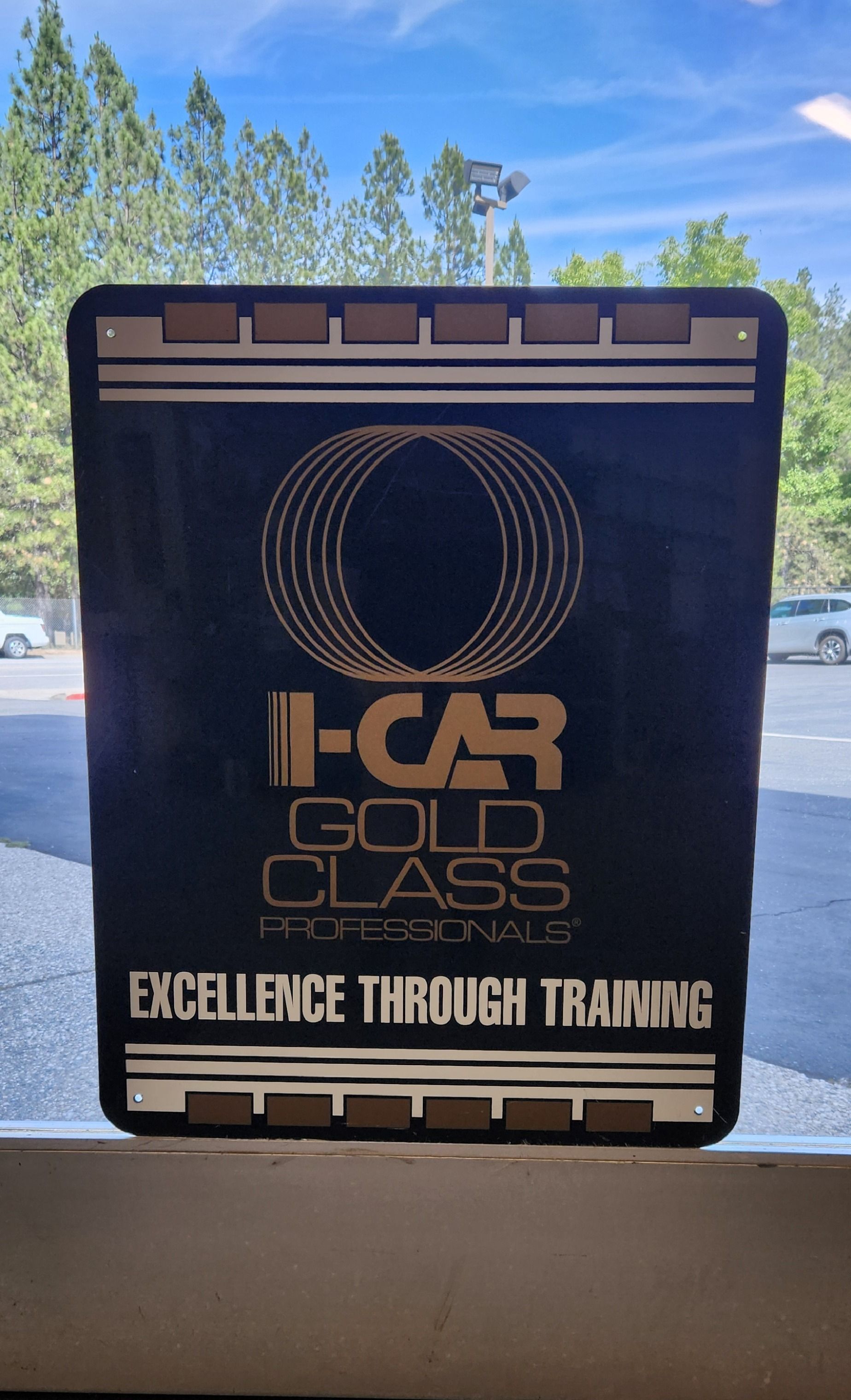Black I-CAR Gold Class sign with logo and “Excellence Through Training” in a window | Tripp's Auto Body