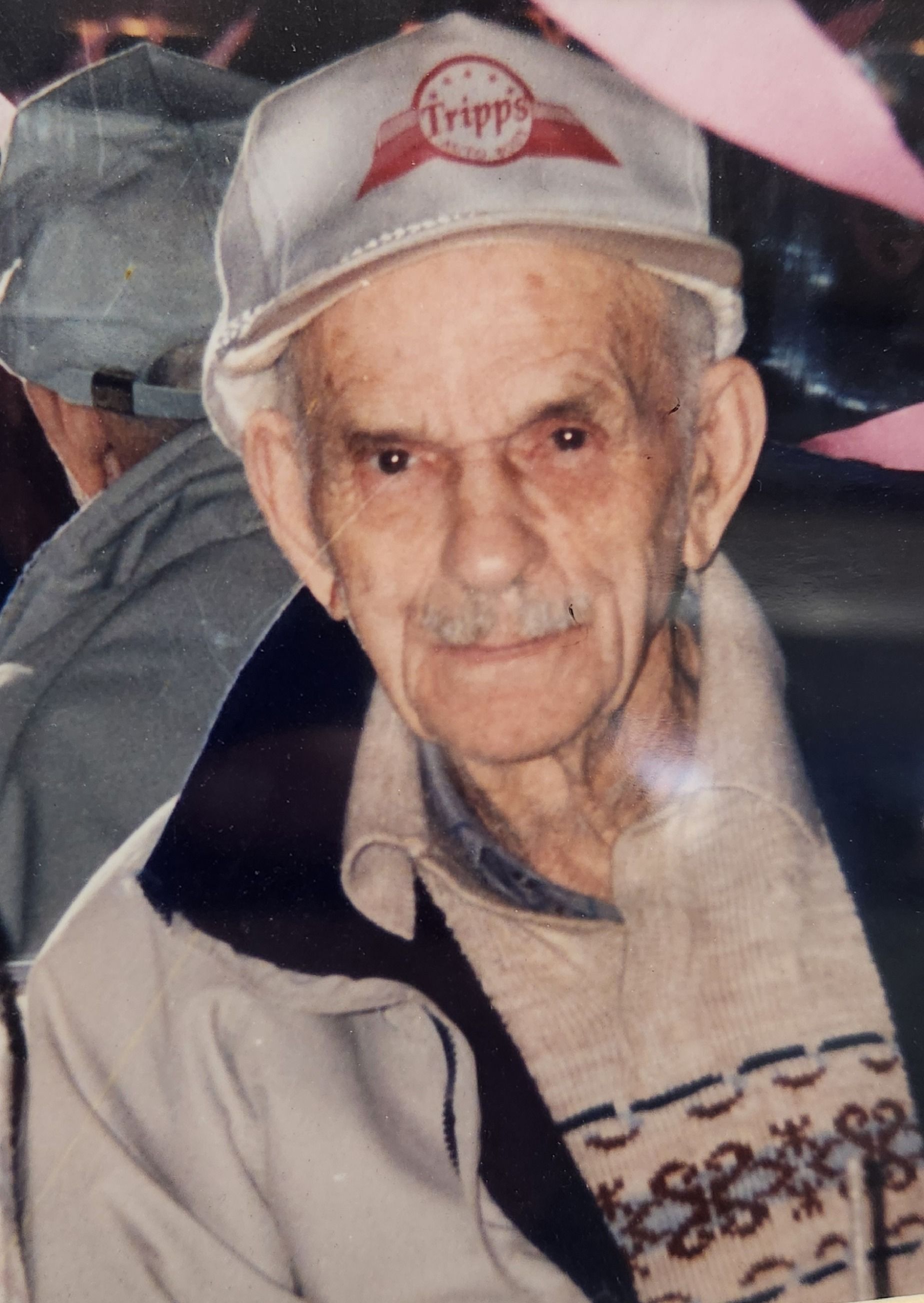 Elderly man in a gray cap and jacket, wearing a patterned sweater, looking at the camera. | Tripp's Auto Body