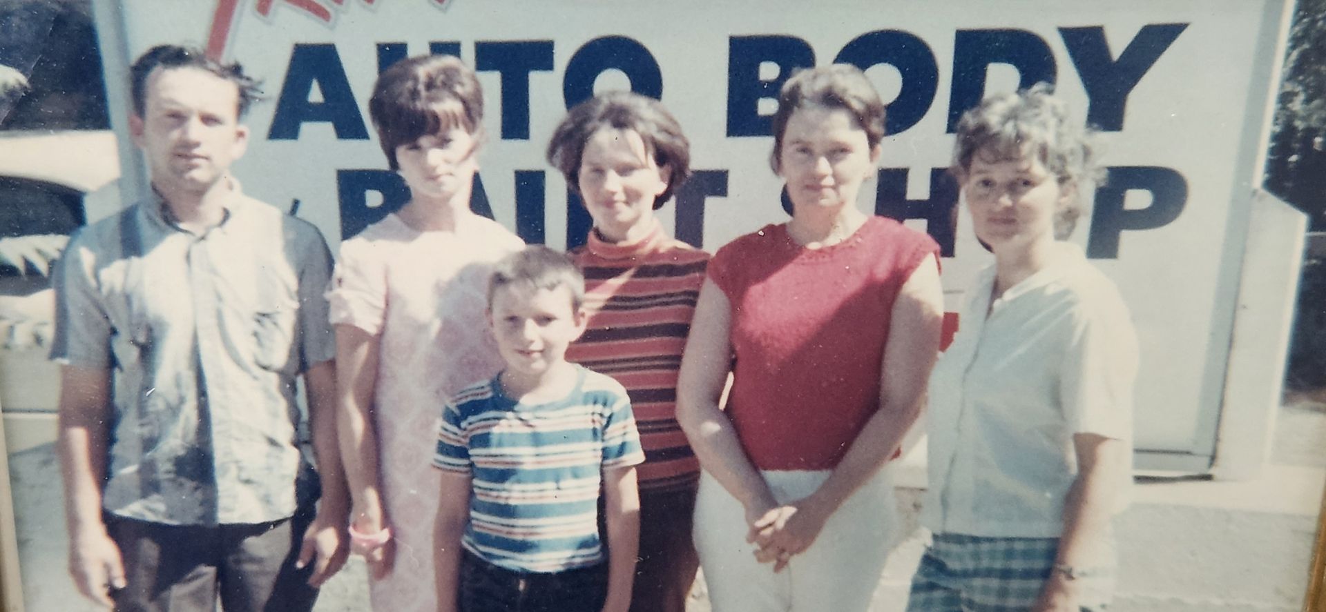 Six people standing in front of an auto body shop sign outdoors. | Tripp's Auto Body