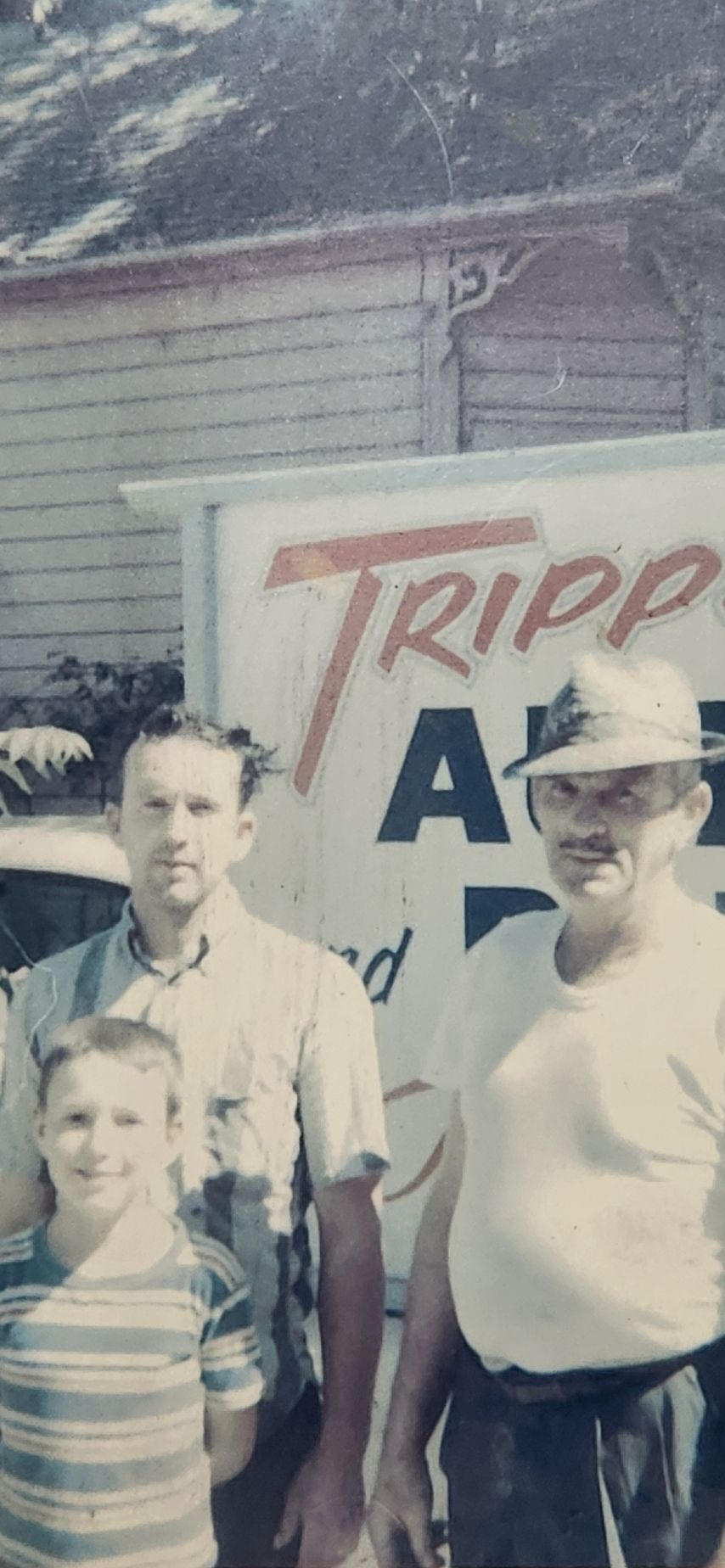 Three people standing in front of a Ripp's sign and a brick building outdoors. | Tripp's Auto Body