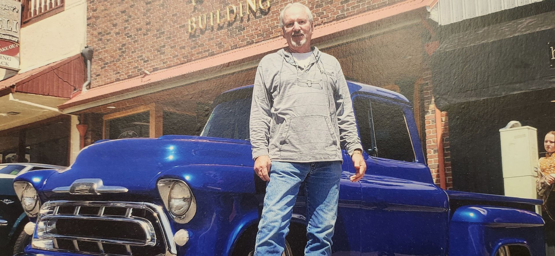 Man standing in front of a blue vintage truck outside a brick building | Tripp's Auto Body