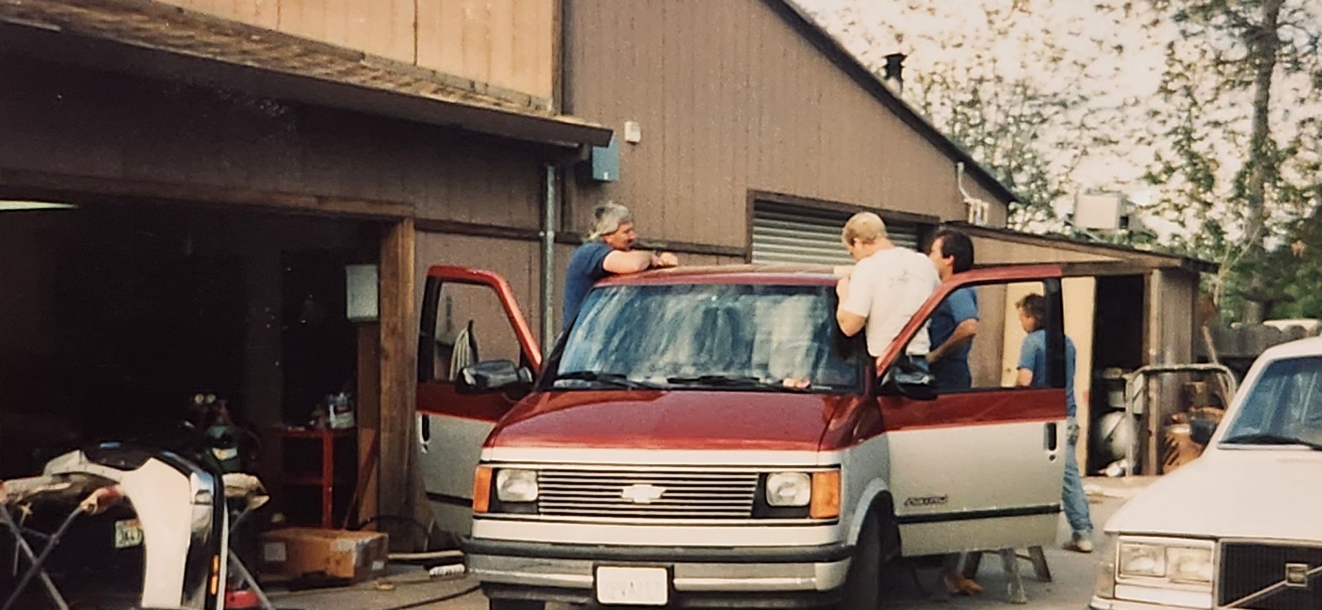 Two people load items into a red van parked in a driveway beside a house and garage. | Tripp's Auto Body