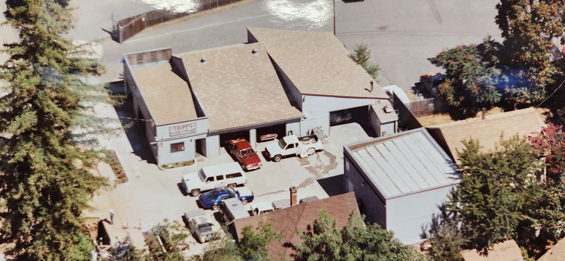 Aerial view of a auto repair shop with a driveway, parked cars, and surrounding trees. | Tripp's Auto Body