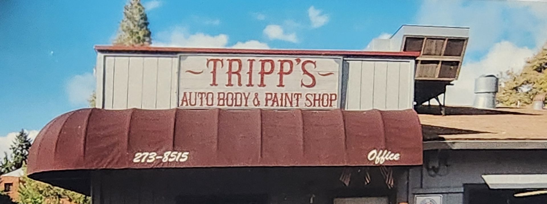 Tripp’s Auto Body & Paint shop with a maroon awning and weathered sign on a sunny day | Tripp's Auto Body