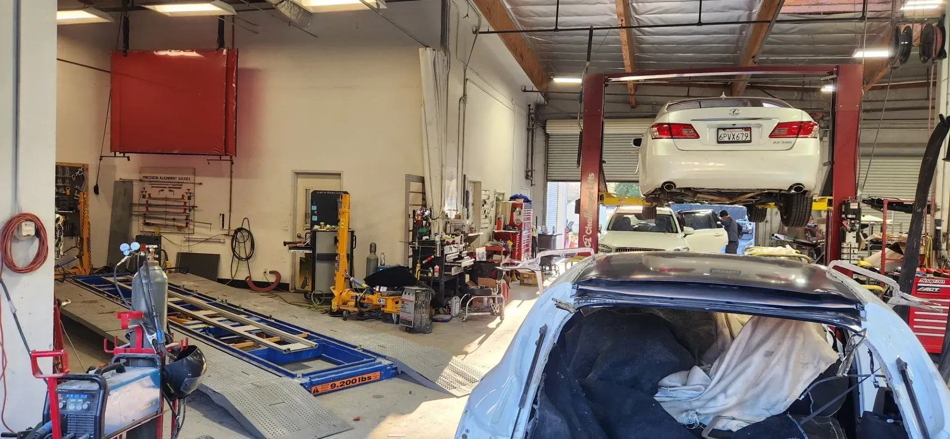 Auto repair garage with cars on lifts, tools on the floor, and a mechanic working in the background | Tripp's Auto Body