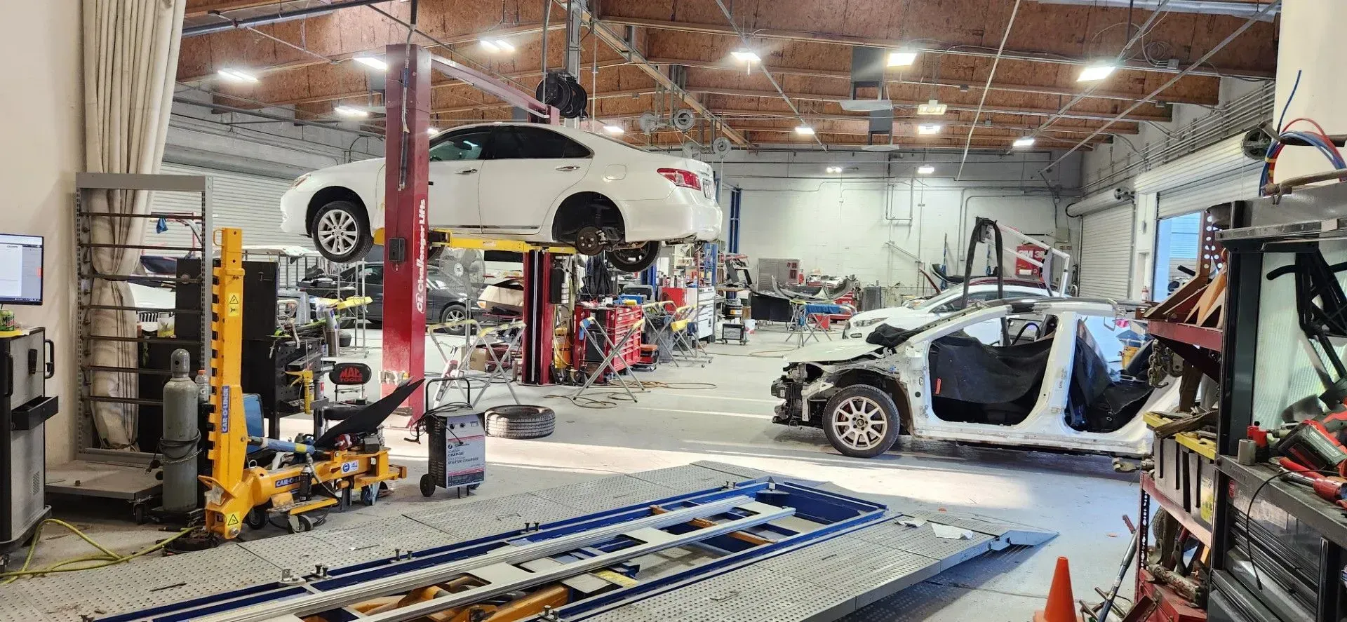 Auto repair shop with a car on a lift and another being worked on, tools and equipment around the garage | Tripp's Auto Body