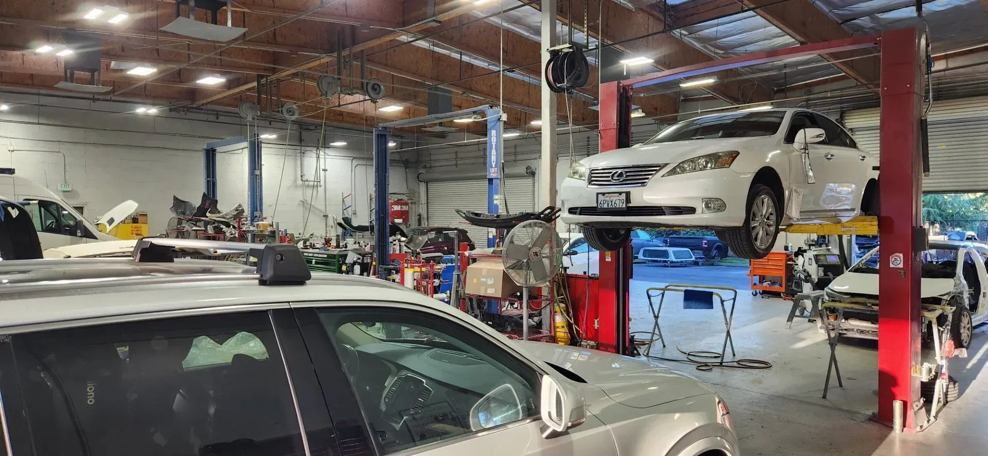 Auto repair shop with cars on lifts and mechanics working under bright workshop lights | Tripp's Auto Body